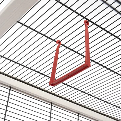 Barre en plastique rouge suspendue au plafond d'une cage à barreaux métalliques noirs, vue rapprochée de l'intérieur de la cage.