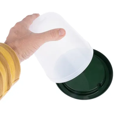 Hand håller en transparent måttbägare med grönt lock, lämplig för dosering av djurfoder.