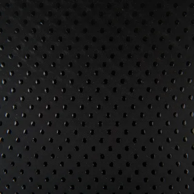Primo piano di una superficie nera perforata con piccoli fori rotondi. Struttura del materiale visibile.