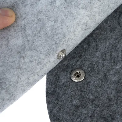 Gros plan sur deux pièces de feutre gris clair et foncé avec bouton-pression métallique visible, montrant le système d’attache du produit.