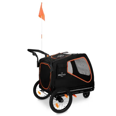 Nomad Tales cykelvagn med svart tyg, orangefärgade detaljer, nätfönster och säkerhetsflagga. Två stora hjul och handtag synliga.