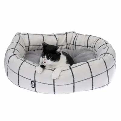 Zwart-witte kat ligt in een geruite, gevoerde kattenmand met grijze voering. Tiaki merklogo zichtbaar aan de voorkant.