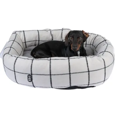 Hond ligt in een wit-grijs geruite hondenmand met TiCK-logo aan de zijkant.
