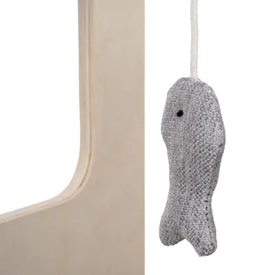 Grey fabric toy in the shape of a fish, hanging on a white string next to a wooden surface.