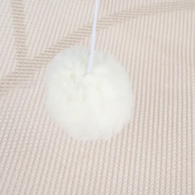 Vit, fluffig boll på snöre på beige matta.