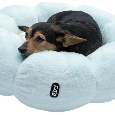 Petit chien allongé dans un panier moelleux en tissu bleu clair, étiquette visible avec la marque Tiaki sur le devant du panier.