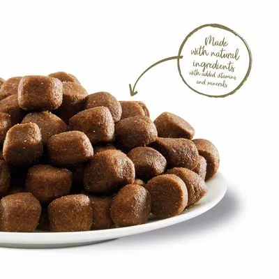 Bord met bruine brokjes. Tekst in beeld: Made with natural ingredients with added vitamins and minerals (Engels).