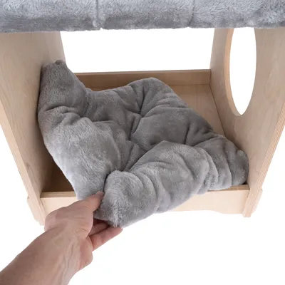 Hand legt ein graues, weiches Kissen in eine Holzkonstruktion mit rundem Eingang. Detailaufnahme des Produkts für Haustiere.