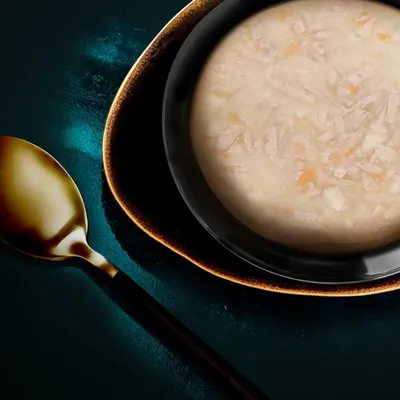 Skål med ljus, fuktig matblandning med synliga bitar, serverad på tallrik bredvid en sked. Ingen synlig text eller varumärke.