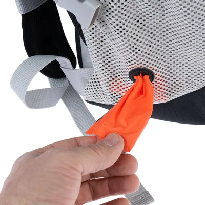 Main tirant un sac orange à travers un distributeur intégré dans une poche en maille blanche avec sangle grise, détail d’un accessoire pour animaux.
