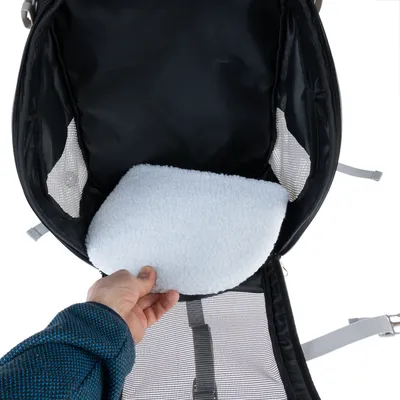 Intérieur d’un sac de transport pour animaux avec coussin amovible en tissu blanc et parois latérales en maille filet. Une main retire le coussin du fond du sac.