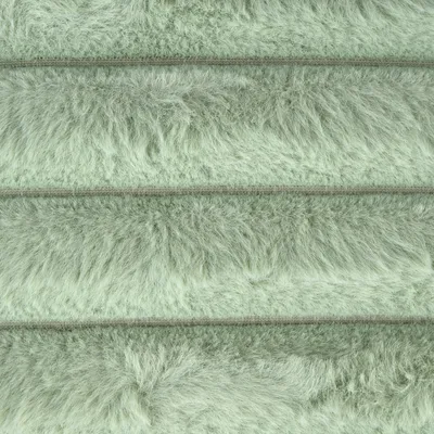 Detailansicht eines flauschigen, hellgrünen Stoffmaterials mit horizontalen Nähten.