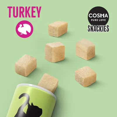 Cosma Pure Love Snackies mit Truthahn, gefriergetrocknete Würfel. Grüner Hintergrund mit Dose und Snacks sichtbar.