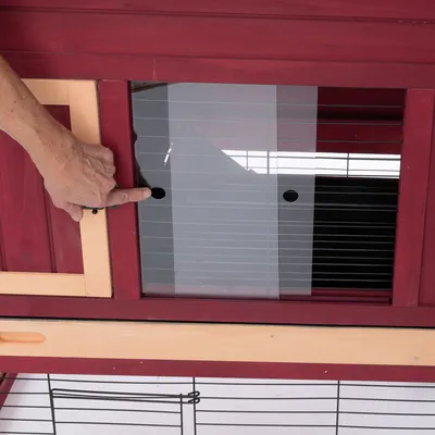 Hand zeigt auf die Schiebetür eines roten Holzgeheges mit Plexiglas und Lüftungsschlitzen.