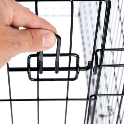 Fermeture en métal noire d'une cage, main tenant le loquet pour ouvrir ou fermer la porte. Structure grillagée visible.