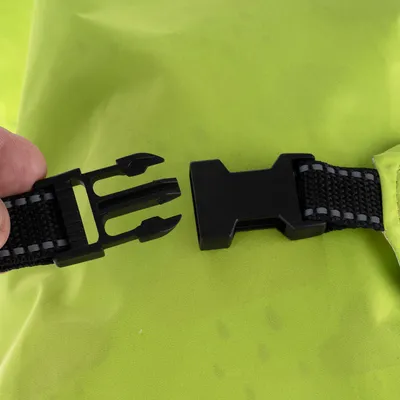 Gros plan sur une attache en plastique noir avec sangle textile noire, devant un tissu vert vif. Une main tient l’un des côtés de l’attache.
