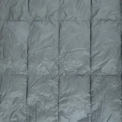 Gråt quiltet tekstil med synlige firkantede syninger, materiale ligner nylon eller polyester. Ingen mærker eller tekst synlige.