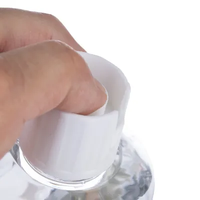 Kéz elforgatja egy átlátszó palack fehér kupakját. A termék nyitásának bemutatása.