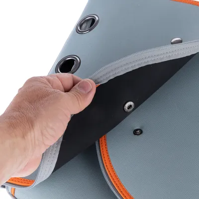 Main soulevant un rabat en tissu gris avec œillets métalliques et bouton-pression sur un sac ou accessoire, détails de couture orange visibles.