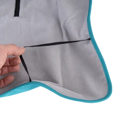 Main tenant une sangle noire fixée à un tissu gris bordé de turquoise, matière polaire visible. Aucun texte ou marque apparente.