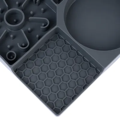 Vue rapprochée d’un plateau en plastique gris avec compartiments de formes variées : alvéoles hexagonales, picots et zone ronde lisse.