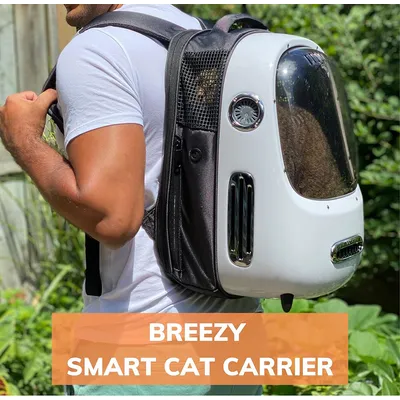 Homme portant un sac à dos de transport pour chat Breezy Smart Cat Carrier, coque blanche avec hublot transparent et aérations visibles. Texte en anglais : Breezy Smart Cat Carrier.