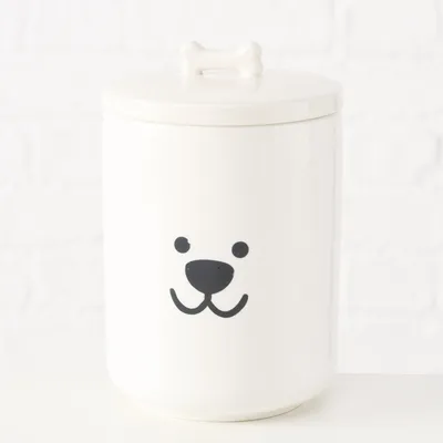 Boîte blanche en céramique avec couvercle orné d’un os et visage de chien dessiné sur le devant, sans marque visible.