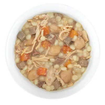 Morceaux de viande, légumes et petites pâtes dans une gamelle blanche, nourriture humide pour animaux visible en gros plan.