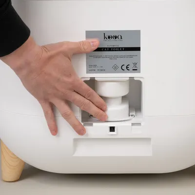 kooa Automatic Cat Toilet with CE marking. Model M001, power 12V-1.5A. Hand shows control area for cleaning or maintenance.