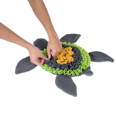 Hände arrangieren Futter in einer grauen und grünen Schnüffelmatte in Schildkrötenform, ideal zur Beschäftigung von Haustieren.