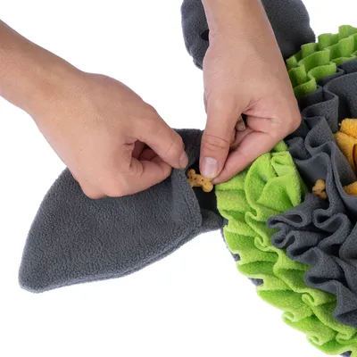 Hände verstecken Leckerlis in einem grauen und grünen Schnüffelteppich aus Stoff.