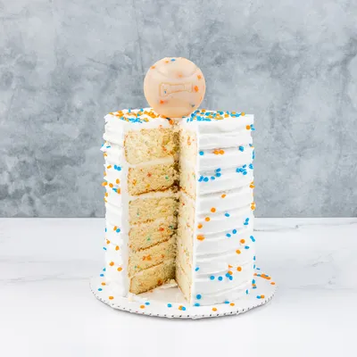 Torta nuziale con glassa bianca, zuccherini arancioni e blu e biscotto rotondo con motivo a osso sopra. Una fetta è tagliata.