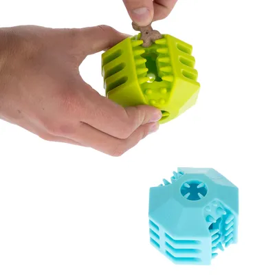 Una mano inserisce uno snack in una palla gioco verde con scanalature. Accanto alla palla verde è visibile una palla gioco blu.