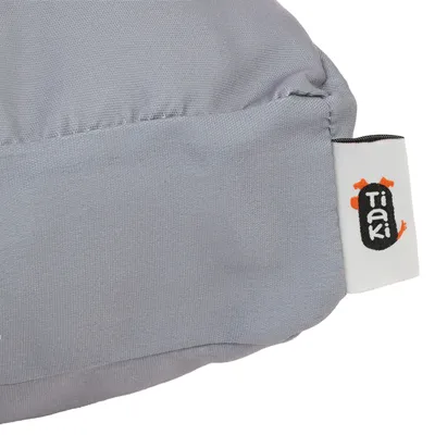 Étiquette blanche avec le texte visible « TIAKI » sur un coussin en tissu gris.