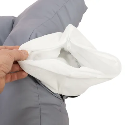 Gros plan sur une main ouvrant la housse grise d’un coussin, révélant un sac intérieur blanc en tissu avec fermeture éclair et rembourrage visible à l’intérieur.