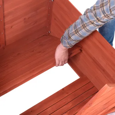 Main retirant une planche amovible du sol d’une niche en bois, montrant l’intérieur et la structure vissée.