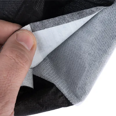 Gros plan sur une main soulevant un coin d’un tissu multicouche gris et blanc, montrant la texture et l’épaisseur des différentes couches du matériau.