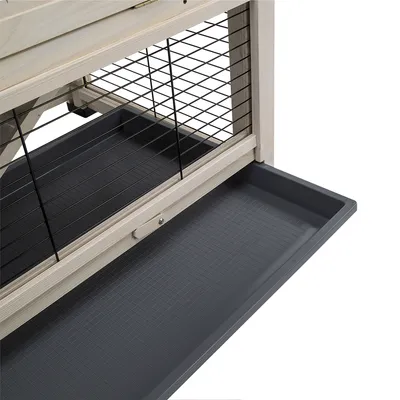 Tiroir amovible en plastique sous une cage en bois et métal, grille noire visible, pour faciliter le nettoyage de l’habitat des petits animaux.