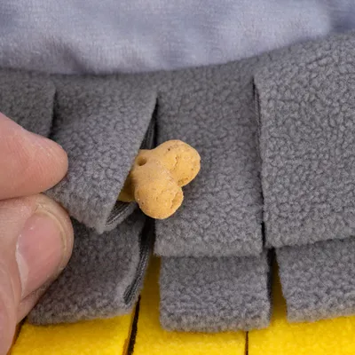 Una mano mette un piccolo biscotto per cani in una borsa di stoffa grigia, parte di un gioco interattivo per la ricerca di snack.
