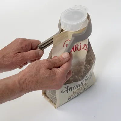 Roka uporablja siv zapiralni sponko z dozirnim pokrovčkom za zapiranje odprte embalaže Ancient Grains Chicken.