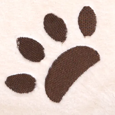 Primer plano de un bordado de pata marrón sobre tela de felpa blanca, posiblemente parte de un producto para mascotas.