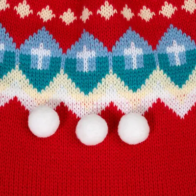 Nahaufnahme eines gestrickten roten Stoffes mit blau-weissen Mustern und drei weissen Pompons als Dekoration.