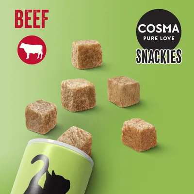 COSMA PURE LOVE SNACKIES BEEF, kostky sušeného masa, vyobrazené s obalem se siluetou kočky na zeleném pozadí. Text 'BEEF' a obrázek krávy vlevo nahoře.