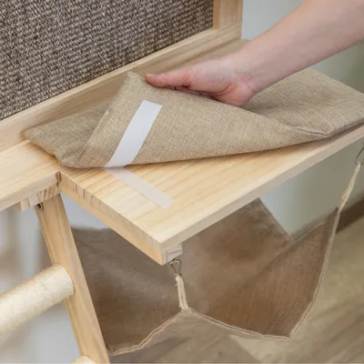 Hand zeigt abnehmbares Kissen mit Klettverschluss auf einer Holzplattform, darunter eine hängende Stofftasche.