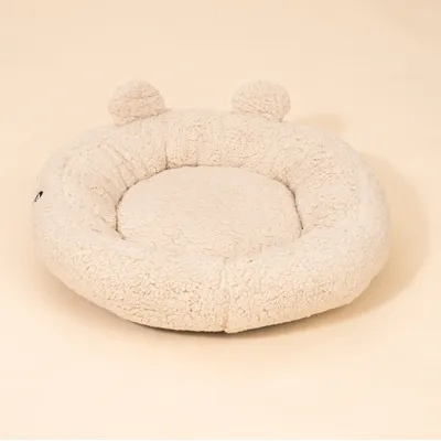 Rundes, beiges Kuschelbett aus Plüsch mit zwei angenähten Ohren. Struktur und Material sind deutlich sichtbar. Rundes, beiges Kuschelbett aus Plüsch mit zwei angenähten Ohren. Struktur und Material sind deutlich sichtbar.