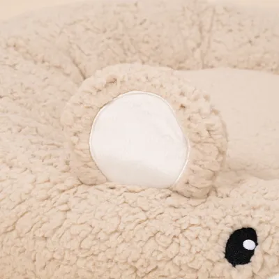 Beiges, flauschiges Bett mit aufgenähter Ohr- und Augenapplikation aus Stoff. Detailaufnahme der Materialstruktur. Beiges, flauschiges Bett mit aufgenähter Ohr- und Augenapplikation aus Stoff. Detailaufnahme der Materialstruktur.