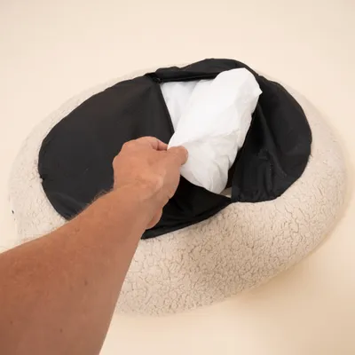 Hand öffnet Reißverschluss an rundem Bett und zeigt herausnehmbares Innenkissen aus weißem Material. Hand öffnet Reißverschluss an rundem Bett und zeigt herausnehmbares Innenkissen aus weißem Material.