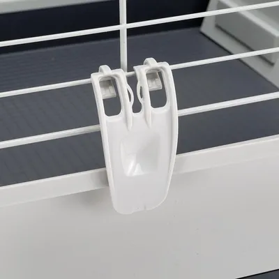 Attache en plastique blanc fixée sur une grille métallique, vue rapprochée du système de fermeture d’une cage pour petits animaux.