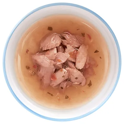 Кусочки мяса в соусе в белой миске с голубым ободком, вид сверху. Видны мелкие овощи и зелень.