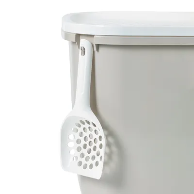 Contenedor gris con tapa blanca y pala para arena blanca colgada en el lateral.